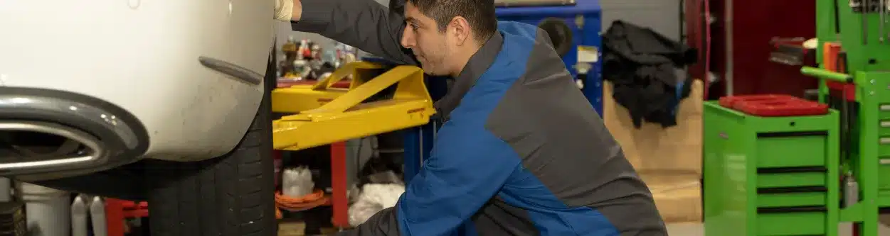 Technician working on a vehicle's tire beside a green tool cabinet in a repair shop.