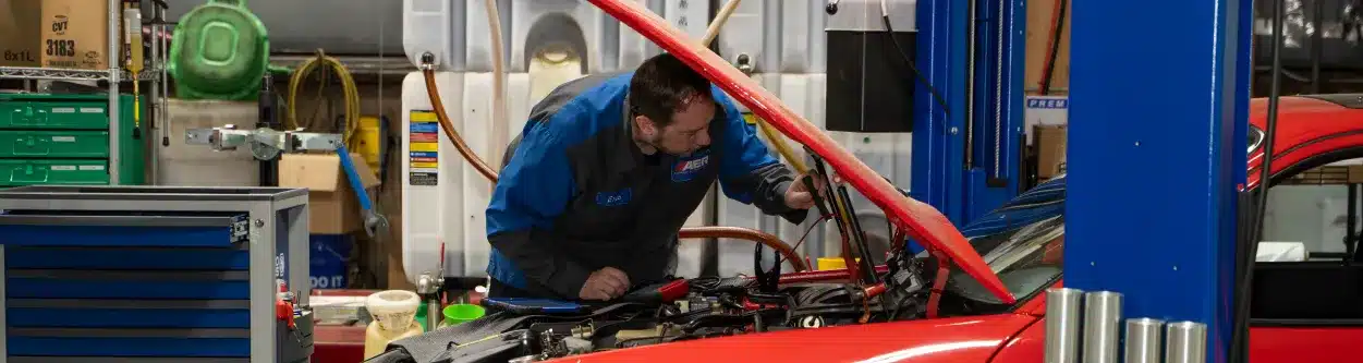 Technician working on a red car in a garage.