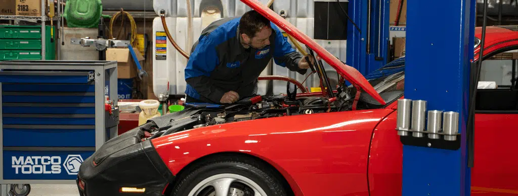Vehicle diagnostics, auto repair in Franklin, MA, at Advanced European Repair. Automotive technician performing vehicle diagnostics on a red European sports car with the hood open, using professional diagnostic equipment to identify engine and electrical system issues.